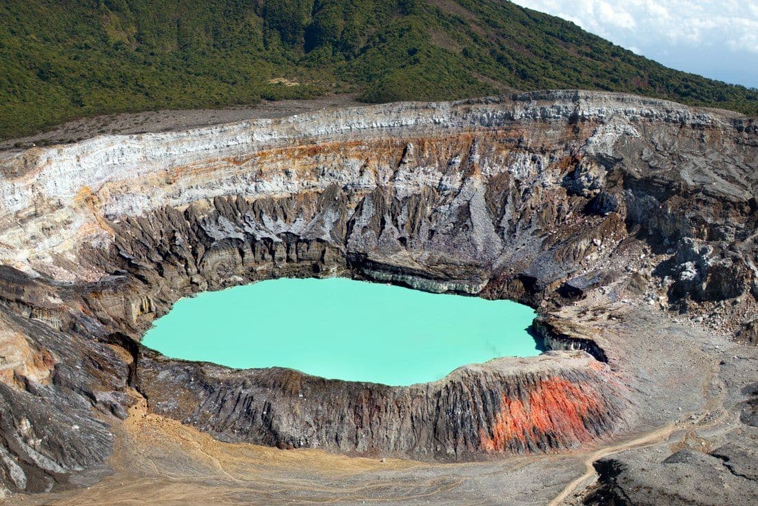 The crater lake at Poás Volcano National Park, a turquoise pool in a gray basin with forest on the slope above.