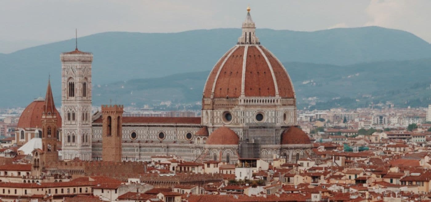 The dome of Florence Cathedral and Giotto's bell tower above the rooftops of Florence, with hills behind.